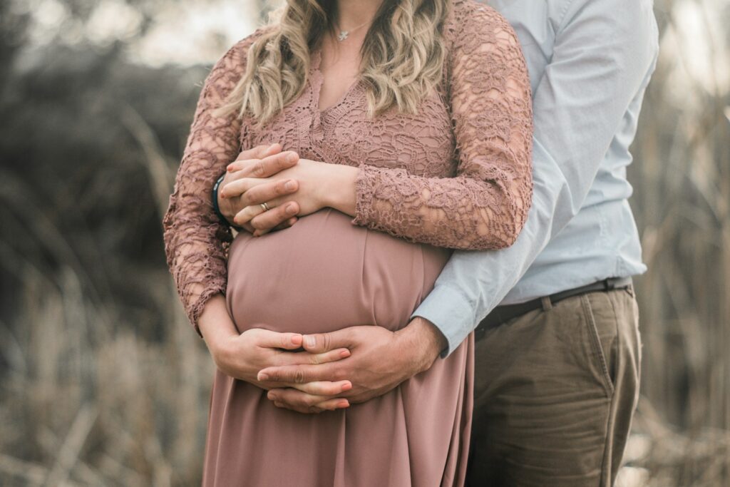 a pregnant couple standing in a field with their hands on their stomachnon riesco a rimanere incinta