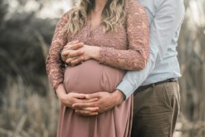 a pregnant couple standing in a field with their hands on their stomachnon riesco a rimanere incinta